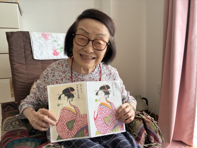 居室で浮世絵の本を手にして笑顔の入居者。文化活動や余暇の様子。