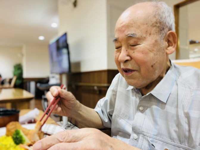 食事中の高齢男性入居者。箸を持って食事を楽しむ様子。