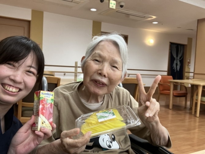 スタッフと入居者がレクリエーション活動中。飲料と菓子を持って笑顔で交流している風景。