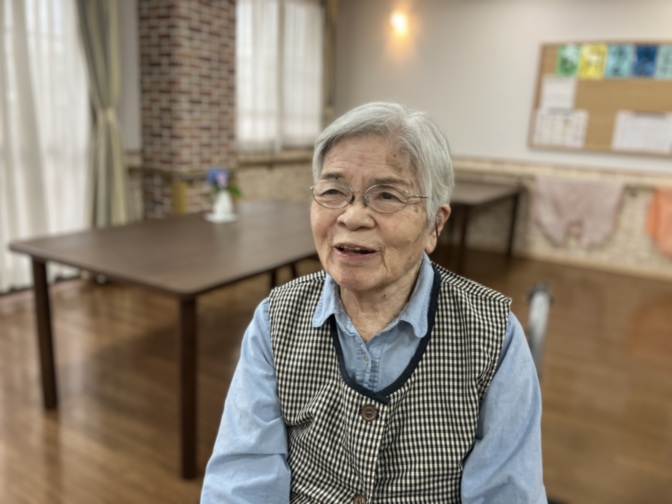 施設の共用スペースにいる高齢者の女性。明るい談話室での日常風景。