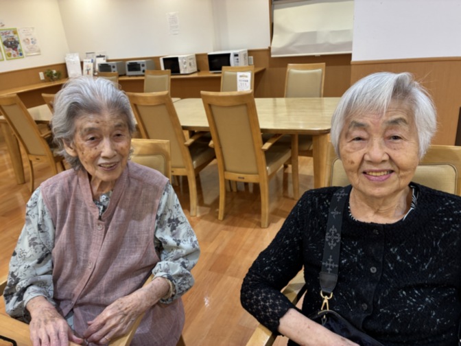 食堂で笑顔の高齢入居者2名。日中の交流風景