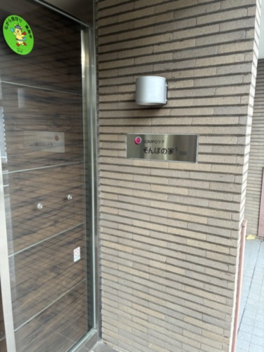 介護施設の玄関入口。ガラス戸と施設名表示板が見える