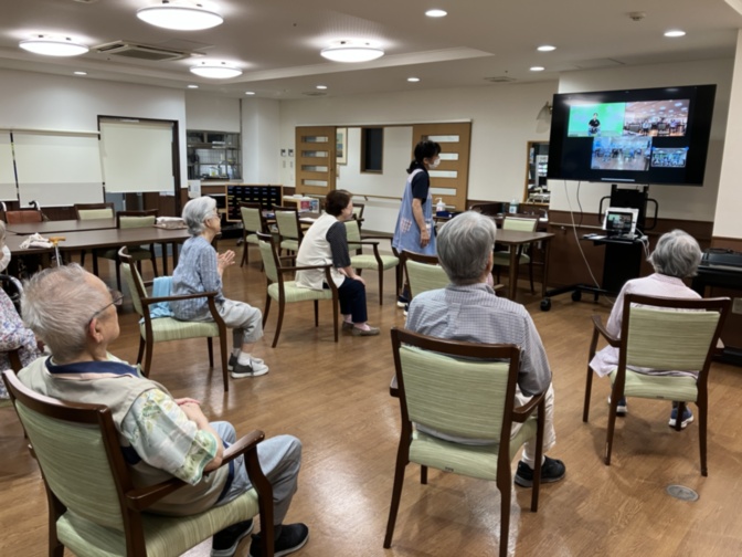 介護施設でのレクリエーション。高齢者が椅子に座ってスクリーン映像を視聴している様子。