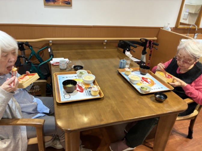 食堂で食事する高齢入居者。木製テーブルで複数名が食事中。