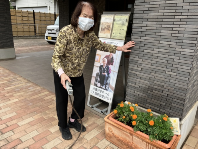 施設入口で案内パネルと花壇の前に立つスタッフ