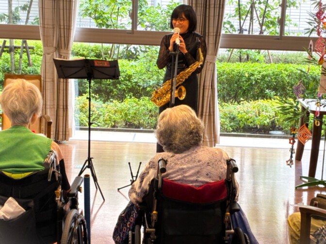 サックス演奏会。入居者が音楽レクリエーションを楽しむ様子。明るい共用スペースで開催。