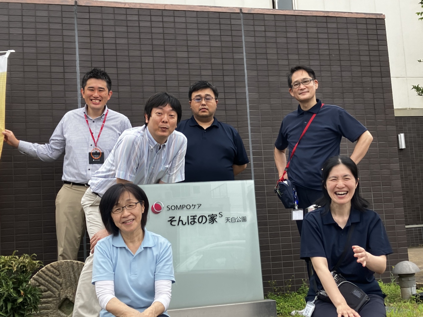 介護施設の職員グループが施設前で撮影した集合写真。名札を着用。