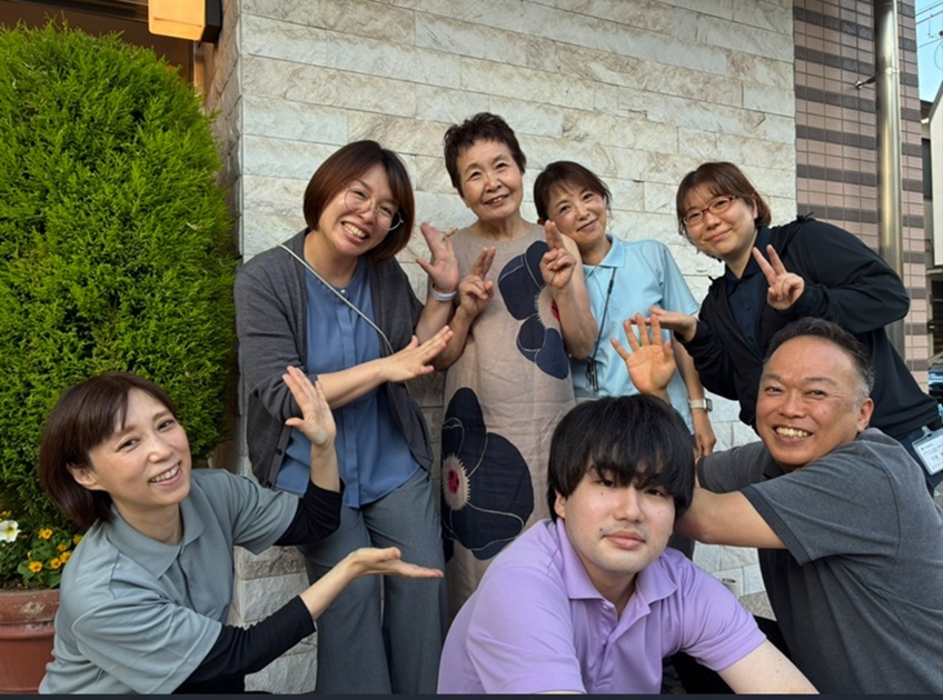 施設スタッフが建物外で集合写真。笑顔でピースサインを見せている
